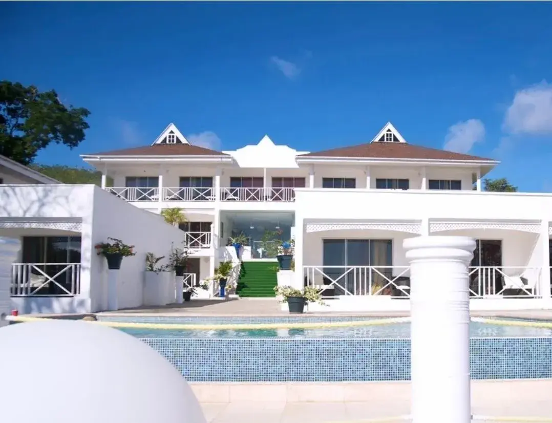 White colonial-style main house rising above the mosaic-tiled pool at Bacolet Beach Club