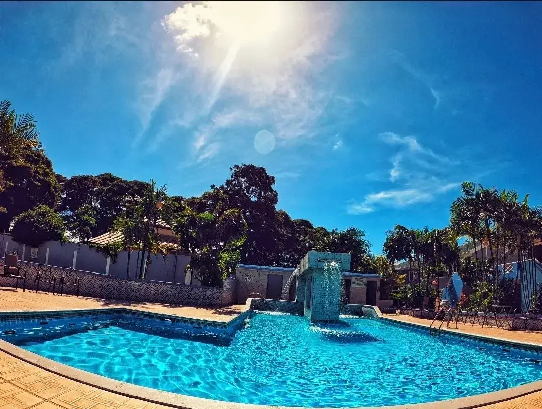 Sun flaring over the palm-lined pool and waterfall feature at Green Palm