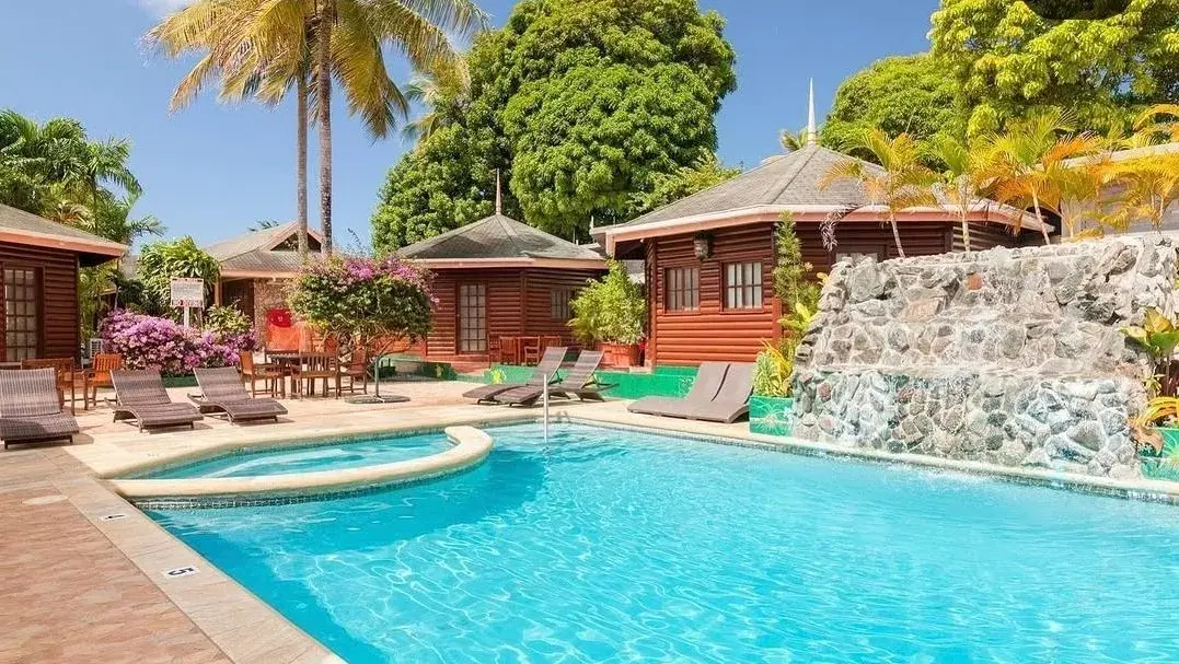 Sunlit pool surrounded by log cabins, palms and bougainvillea at Shepherd's Inn
